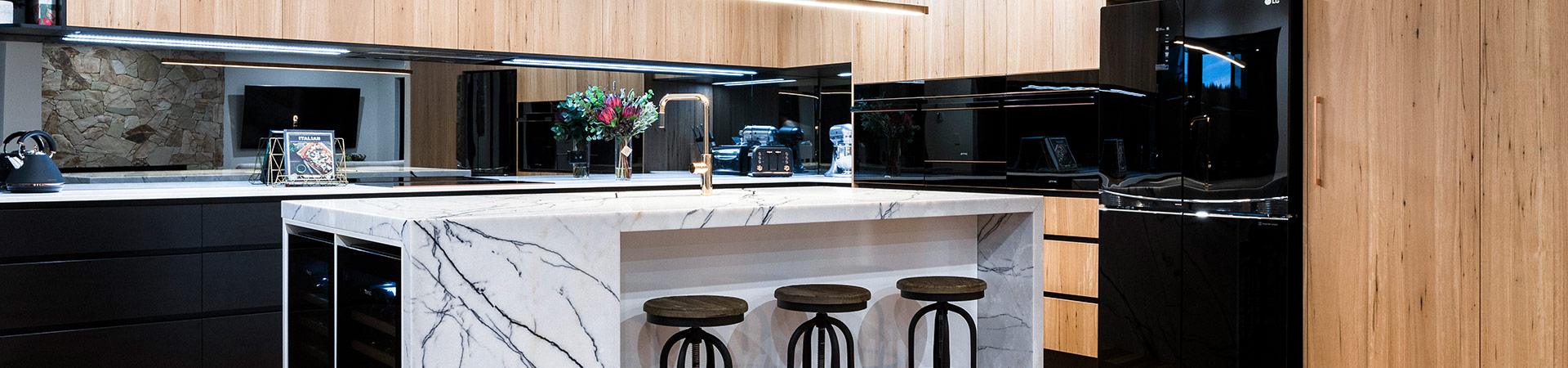 Flexi Renovations Perth Modern luxury kitchen featuring marble waterfall island, black gloss cabinetry, light timber panels, and mirrored splashback