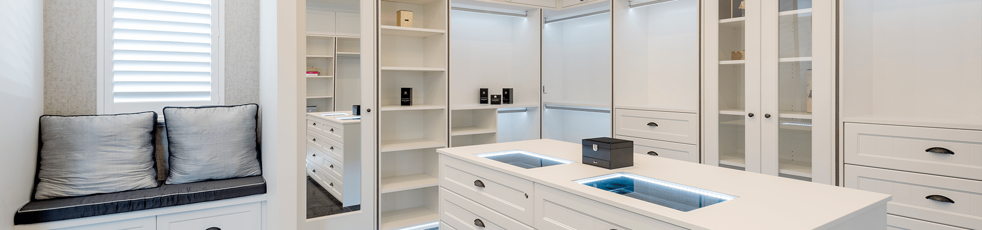 Flexi Renovations Perth Luxurious white custom walk-in wardrobe with built-in shelving, drawers, centre island and window seat bench in Perth home