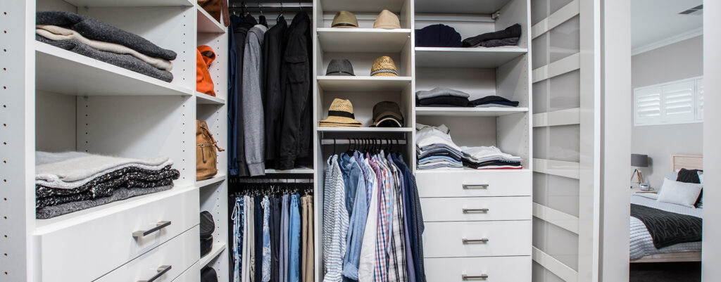 Spacious walk-in wardrobe in Iluka featuring shelves, drawers, hanging clothes, and hats, maximizing storage.