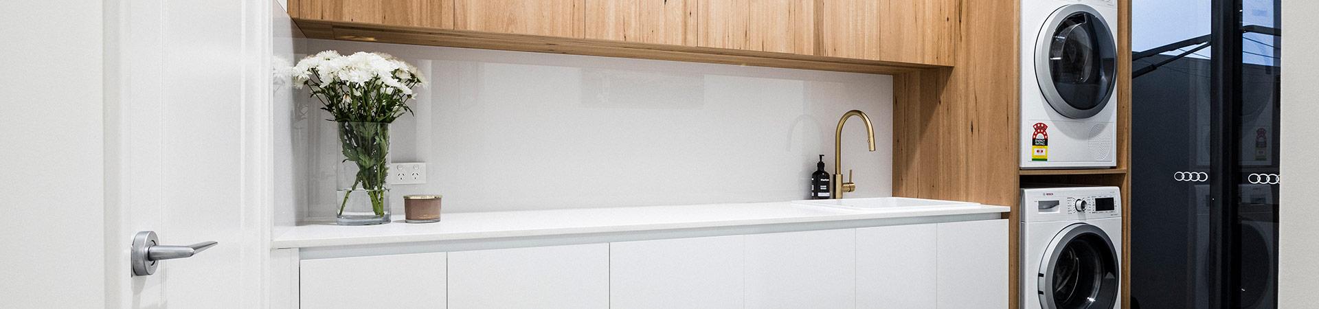 Flexi Renovations Perth Modern luxury laundry renovation featuring white countertops, timber cabinetry, gold tapware, and stacked Bosch washer dryer
