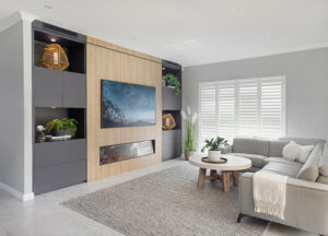 Coastal family room in Ocean Reef with custom built-in shelves, fireplace, and gray sectional sofa. Modern interior design.