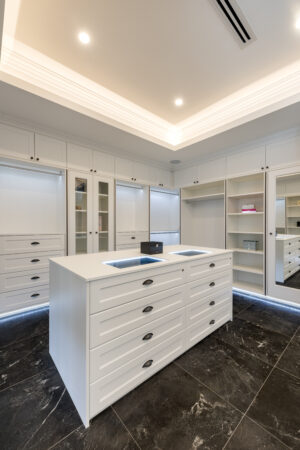Refined Hamptons style walk-in closet in Dalkeith with custom white cabinetry and black marble flooring.