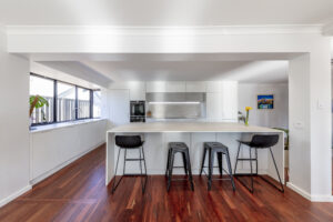 Modern Coastal kitchen in Kallaroo featuring a large island, white cabinets, and sleek black bar stools.